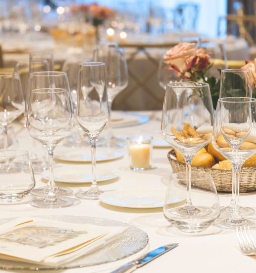 A formal dining table set with multiple wine glasses, plates, cutlery, candles, and a bouquet of peach roses for a elegant event.