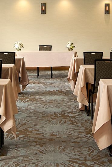 A conference room set up for a formal meeting with rows of tables covered in beige tablecloths, chairs, and small floral centerpieces, facing a head table.