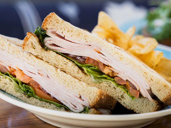 A classic club sandwich with toasted bread, sliced turkey, lettuce, tomato, and mayo, served on a plate with chips on the side.