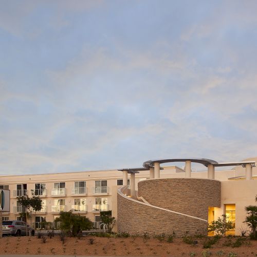 A small desert town with low beige buildings under a blue sky, and a few palm trees along a street.
