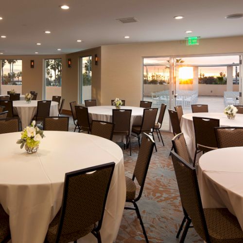 A banquet hall with round tables, white tablecloths, chairs, and a few decorative centerpieces under bright ceiling lights.
