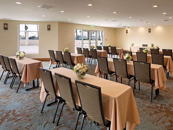 A conference or banquet room set up with long tables draped in peach tablecloths, flowers at centerpieces, and rows of chairs for a meeting or event.