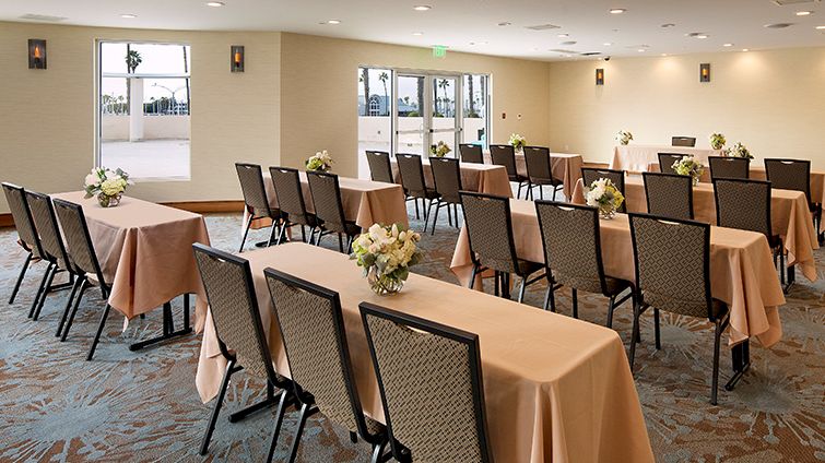A conference or banquet room set up with long tables draped in peach tablecloths, flowers at centerpieces, and rows of chairs for a meeting or event.