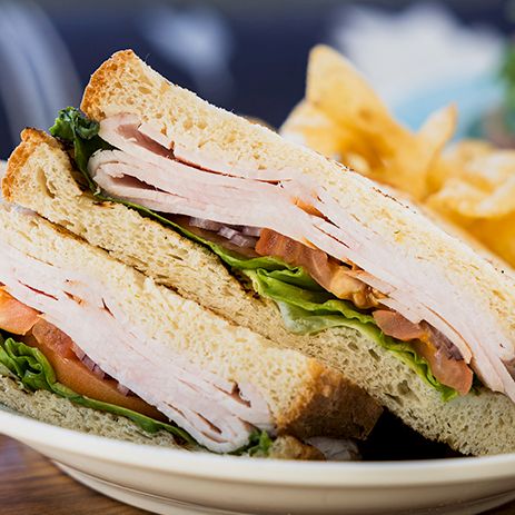 A turkey club sandwich: stacked toast with turkey, lettuce, tomato, and mayo, served with potato chips on the side.