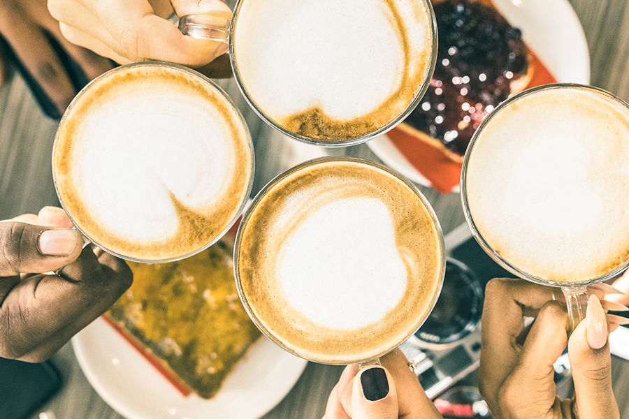A cheerful group cheers with latte art-topped coffees, toasting friends over a shared brunch.